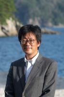 海を後ろにして浜辺でほほえむ男性を正面から写した写真