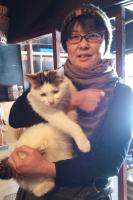 1匹の猫を両手で抱えて笑顔を見せる女性を正面から写した写真