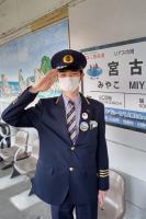 鉄道会社の制服を着て、ぴんと伸ばした片手をこめかみ辺りにそえて敬礼のポーズをとっている男性を正面から写した写真
