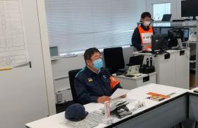 消防活動服を着た市長が椅子に座り、机の上の資料を手に持っている写真