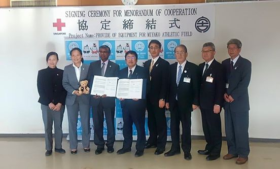 バックパネルの前で締結書を広げて持つ市長とシンガポール赤十字社のベンジャミン・ウィリアム事務局長と関係者の方々の記念写真