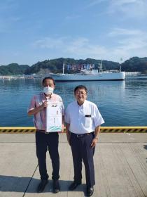 大きな船が停泊している港で、市長と男性が立ち並んでいる写真