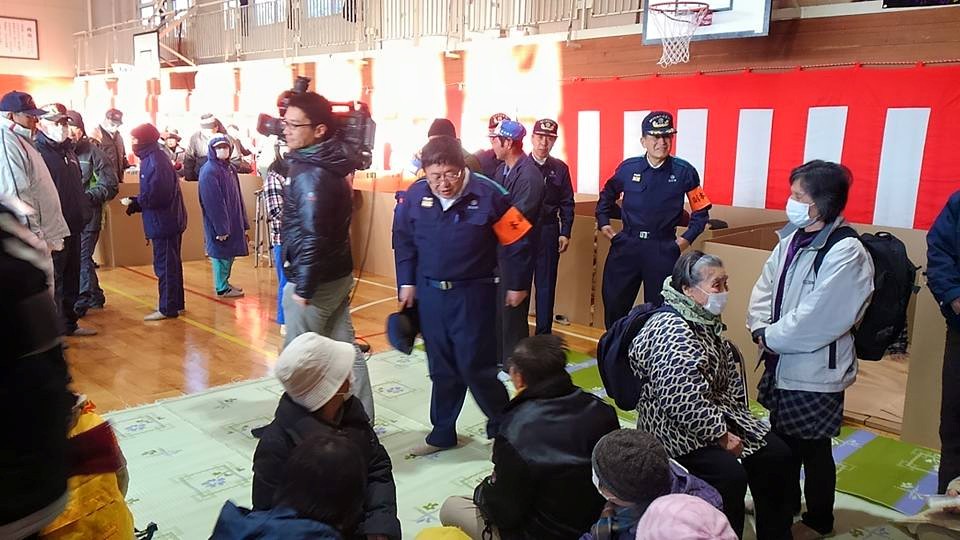 紺色の作業服を着てオレンジ色の腕章をつけた市長が、避難所を視察している様子の写真