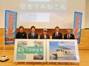 宮古うみねこ丸の写真パネルの後ろで、制帽をかぶった市長と関係者5名が並んでいる写真