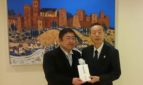 品川区の桑村正敏副区長から白の胸章をつけた市長へ義援金の目録を渡されている写真