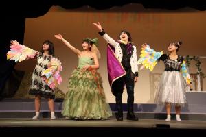 舞台上で衣装を身にまとった役者4名が片手を斜め前にあげ演技をしている写真