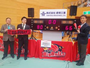 デジタルスコアボードの前で市長と関係者2名がタオルやメガフォンを持ち記念撮影している写真