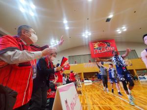 体育館内でユニホームを着た市長が観客席から歩いている選手に手を振っている写真