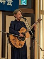 スタンドマイクの前に立ちギターを持ちながら歌を歌っている女性の写真