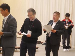 黄色の着物をきた小田代直子さんと半被をきた市長を含めた男性5名がステージ上に立ち紫色のライトで照らされている写真