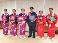 浴衣を着て団扇を持つ市長と4名の男女、紺色の洋服を着て団扇を持った関係者1名が横一列に並ぶ記念写真