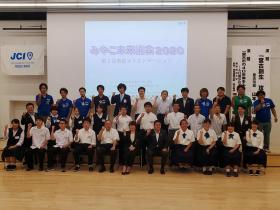 スクリーンの前で3列に整列し右手の拳を顔の横に掲げポーズをとっている市長とみやこ未来議会2020の参加者の方々の写真