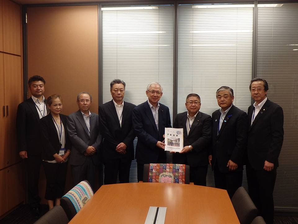 ブラインドカーテンが掛かった窓ガラスの前で要望書を一緒に持つ市長と男性と男性5名、女性1名が横一列に並んでいる記念写真