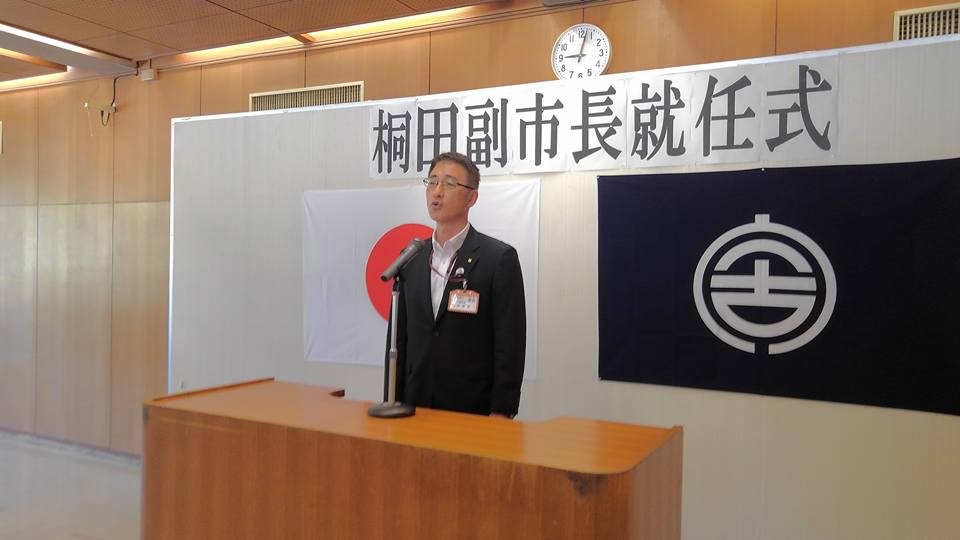 「桐田副市長就任式」と書かれた紙と日本国旗、宮古市の市町村旗が貼られたボードの前に置かれた演台で話をする様子の桐田副市長の写真