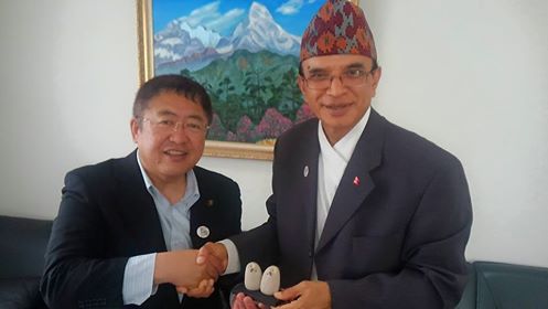 右手で置物を一緒に持ち、左手で握手をする市長とネパール大使館の関係者の男性の記念写真