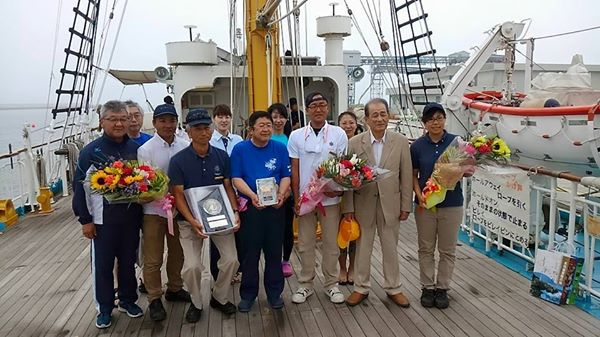 船の甲板で花束や盾を持つ関係者の方々の中心に市長が立って並んでいる記念写真
