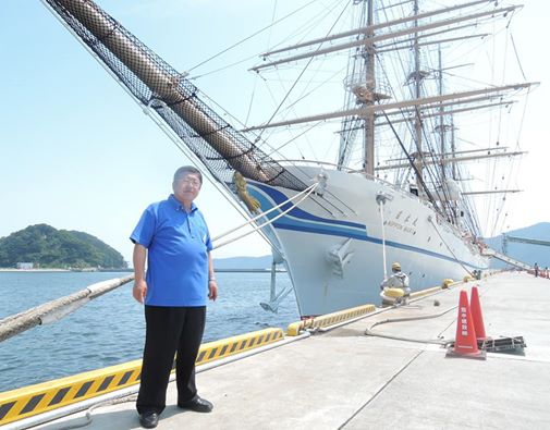 帆船「日本丸」を背に立つ青いポロシャツを着た市長の写真