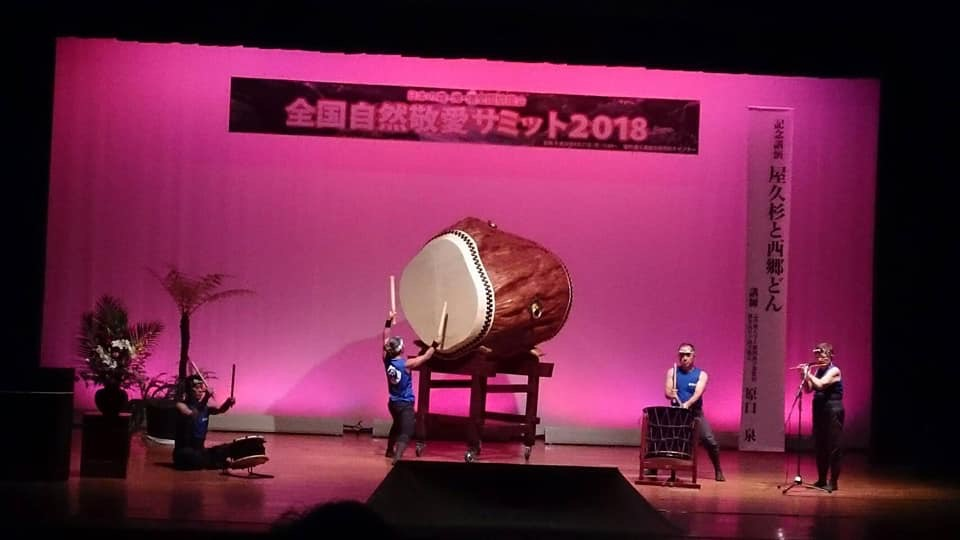 ピンク色にライトアップされた舞台上で、大太鼓や太鼓を演奏する方々の写真