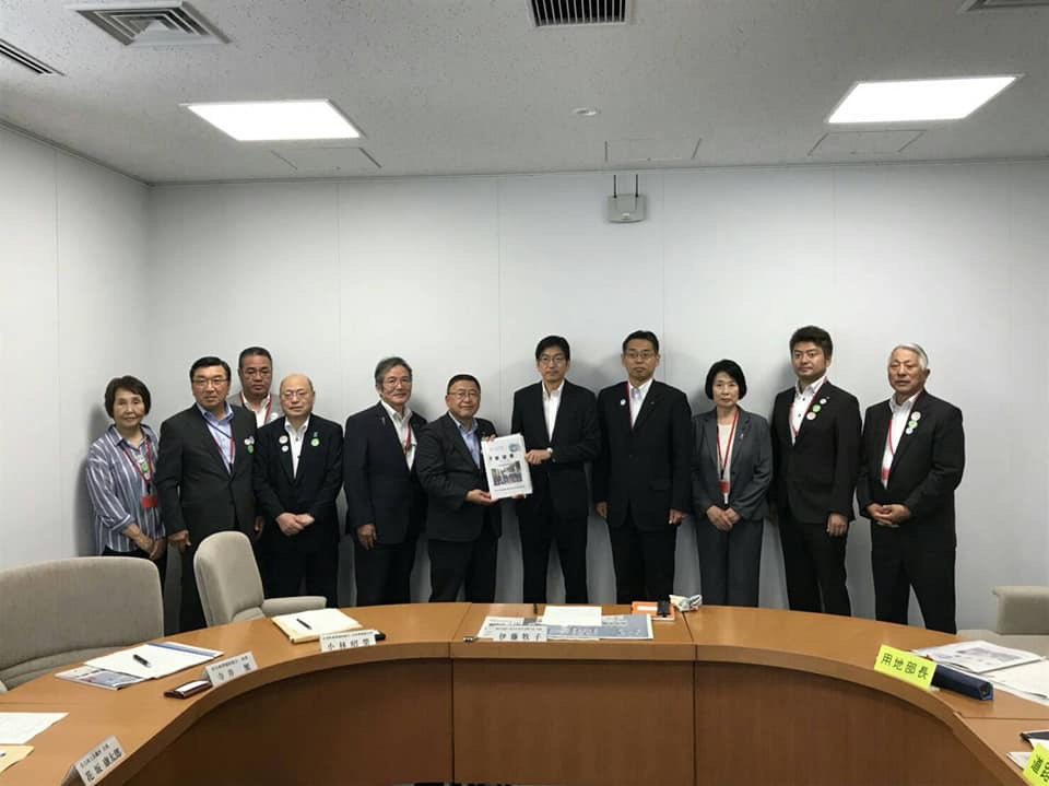 円形のテーブルが置かれた部屋の壁際で、要望書を持つ市長と男性を中心に、女性2名と男性7名が横一列に並んでいる記念写真