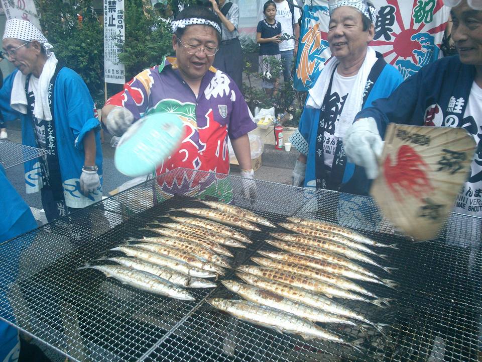 網の上に並べられたサンマを団扇で仰ぐ様子の市長の写真