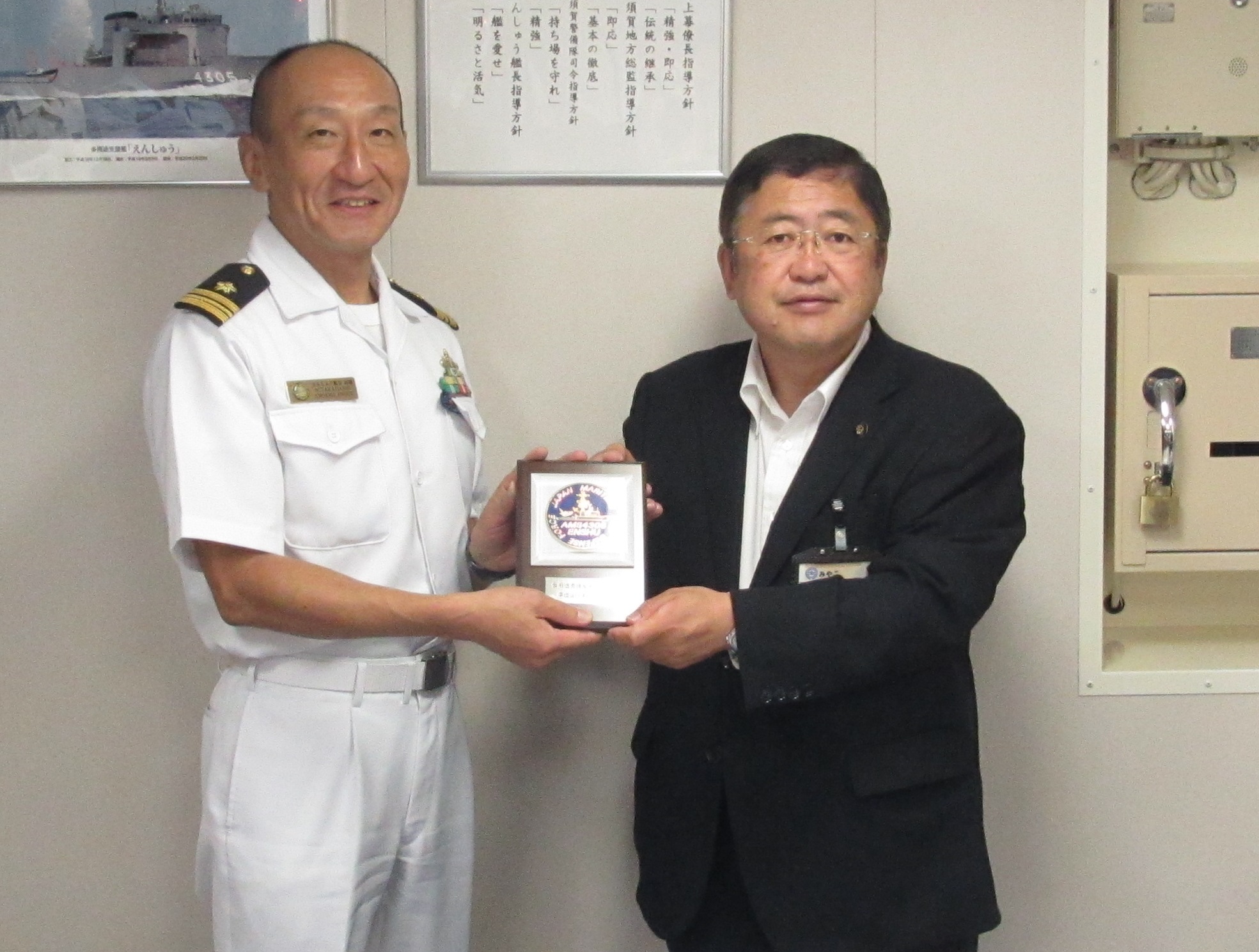 小さな盾を一緒に持つ市長と海上自衛隊の白い制服を着た男性の写真