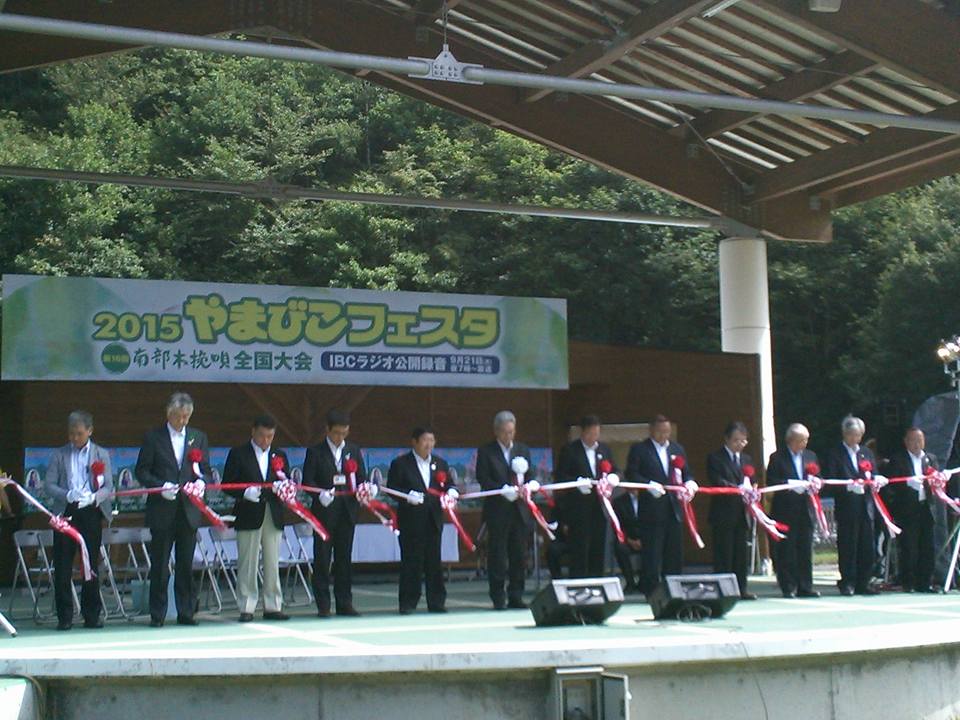 「2015やまびこフェスタ」と書かれた看板が掲げられた舞台上で、テープカットをする市長と関係者の方々の写真