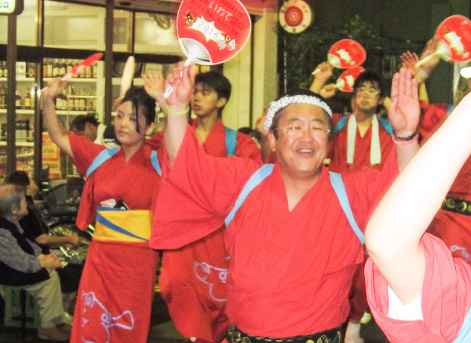 赤い浴衣を着て団扇を持つ市長や参加者の方々が両手を上げて踊っている様子の写真