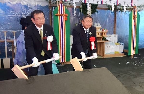 胸章を着けた市長と男性が、盛り土に鍬入れをしている様子の写真