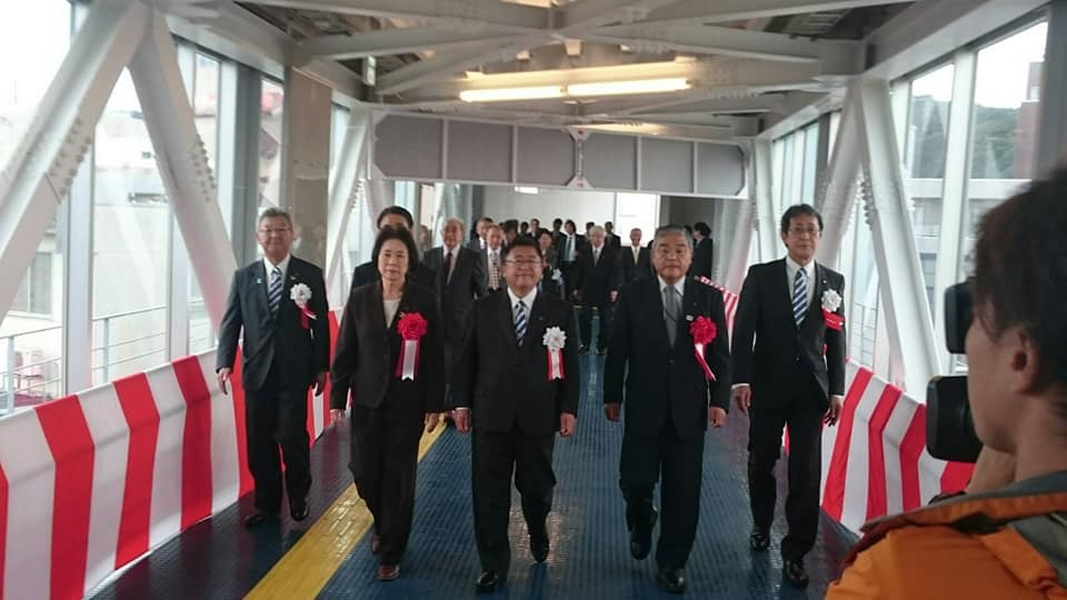 左右の壁に紅白幕が貼られた通路の中央を横一列になって歩く様子の市長と関係者の方々の写真