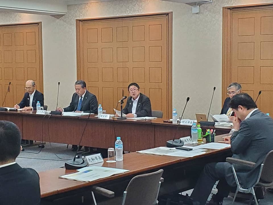 L字型に並べられた席に座る委員会の参加者とマイクに向かって話をしている様子の市長の写真