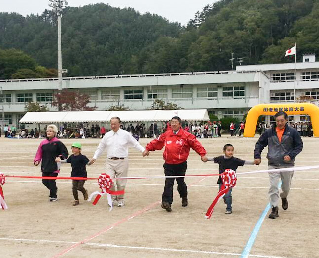 市長と男性2名、女性1名、子供2名が手をつないで赤と白のゴールテープに向かって走る様子の写真