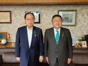 絵や賞状の額縁が飾られた壁の前で並んで立つ土田正剛市長と山本市長の写真