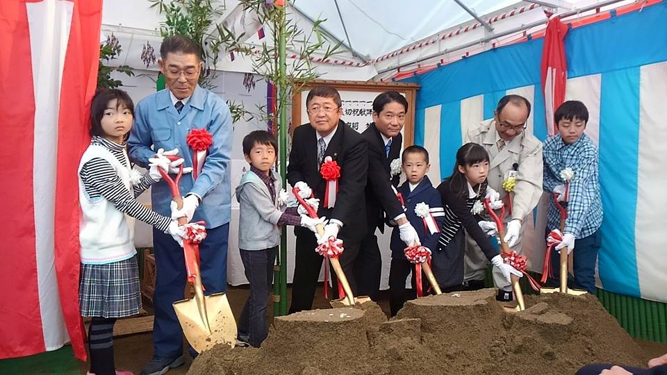 テントの中で盛り土にスコップで鍬入れをする様子の市長、関係者の男性4名、子供5名の写真