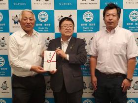 義援金の封筒を一緒に持つ市長と男性、その隣に立つ男性1名の記念写真