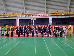 「三陸沿岸道路 仙台~八戸 全線開通」と書かれた横断幕やくす玉が飾られた会場で、関係者や6体のマスコットキャラクターが並ぶなかテープカットが行われている開通式の様子の写真