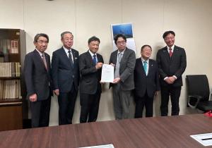 本棚や壁にカレンダーが掛けられた室内で、人事局人事政策統括官の阪本克彦氏と静岡市長の難波喬司氏が一緒に要望書を持ち、ブロック幹事の宮古市長と3名の市長が横一列に並んでいる写真