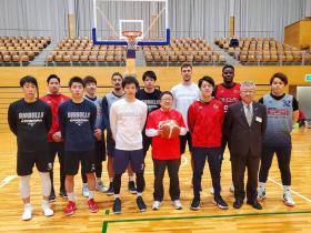 体育館で赤のユニフォームを着て、バスケットボールを持った市長と 岩手ビッグブルズの選手が集合している写真