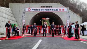トンネル入口前に開通を祝う幕の下で割られているくす玉を背景に、レッドカーペットで市長の他6人でテープカットをしている写真