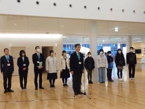 8名の小中学生のみなさんと3名の関係者の方々が1列に並び、その前に設置されたマイクスタンドに1人の男性が立っている「見送り式」での写真