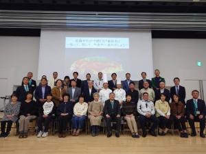 資料が写されたおおきなスクリーンの前に関係者30名程が3列に並んだ集合写真