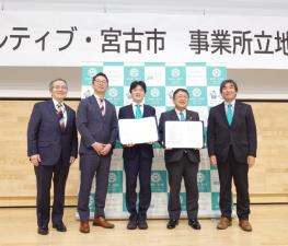 「カルディブ・宮古市事業所立地協定」と書かれたバックパネルの前で市長含めた関係者5名が並んでいる写真