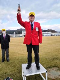 開催会場で市長が黄色の帽子を被り、赤色のジャッケトを着て、右手を挙げてスターターをしている写真