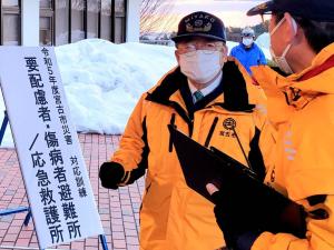 「要配慮者・傷病者避難所・応急救護所」の前でお揃いのオレンジの服を着た市長と関係者の方が話をしている津波避難訓練時の写真