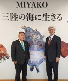 MIYAKO三陸の海に生きると書かれたパネル背景の前で、黒色のスーツを着た武田俊彦さんと市長が並んでいる写真
