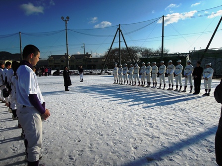 雪で埋め尽くされたグランドで野球服をきた学生たちが向かいあっている写真