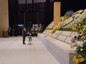 追悼式で市長が多くの花で飾られた祭壇の前に立ち、式辞を述べている写真