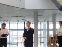 外が見える室内で、市長がマイクスタンドの前に立ち話をしている写真