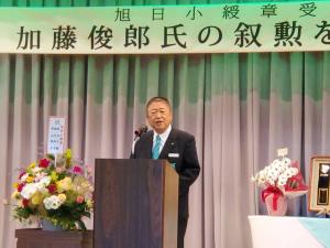 横断幕が張られて、お祝いの花が飾られた演台で市長が祝辞を述べている写真