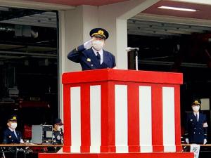 紅白幕の演説台に消防団の制服を着た男性が敬礼している写真