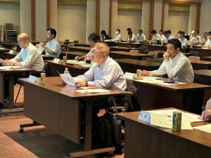 全国市長会第12回防災対策特別委員会で席に座り資料を手に持って前方を向いている市長の写真